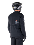 Vista trasera de un piloto con la chaqueta Alpinestars AMT-8 Stretch Drystar® XF en negro, con el logotipo 'AMT Alpinestars Motion Technology' en la espalda y ventilación técnica con cremallera, combinada con casco y guantes de moto negros