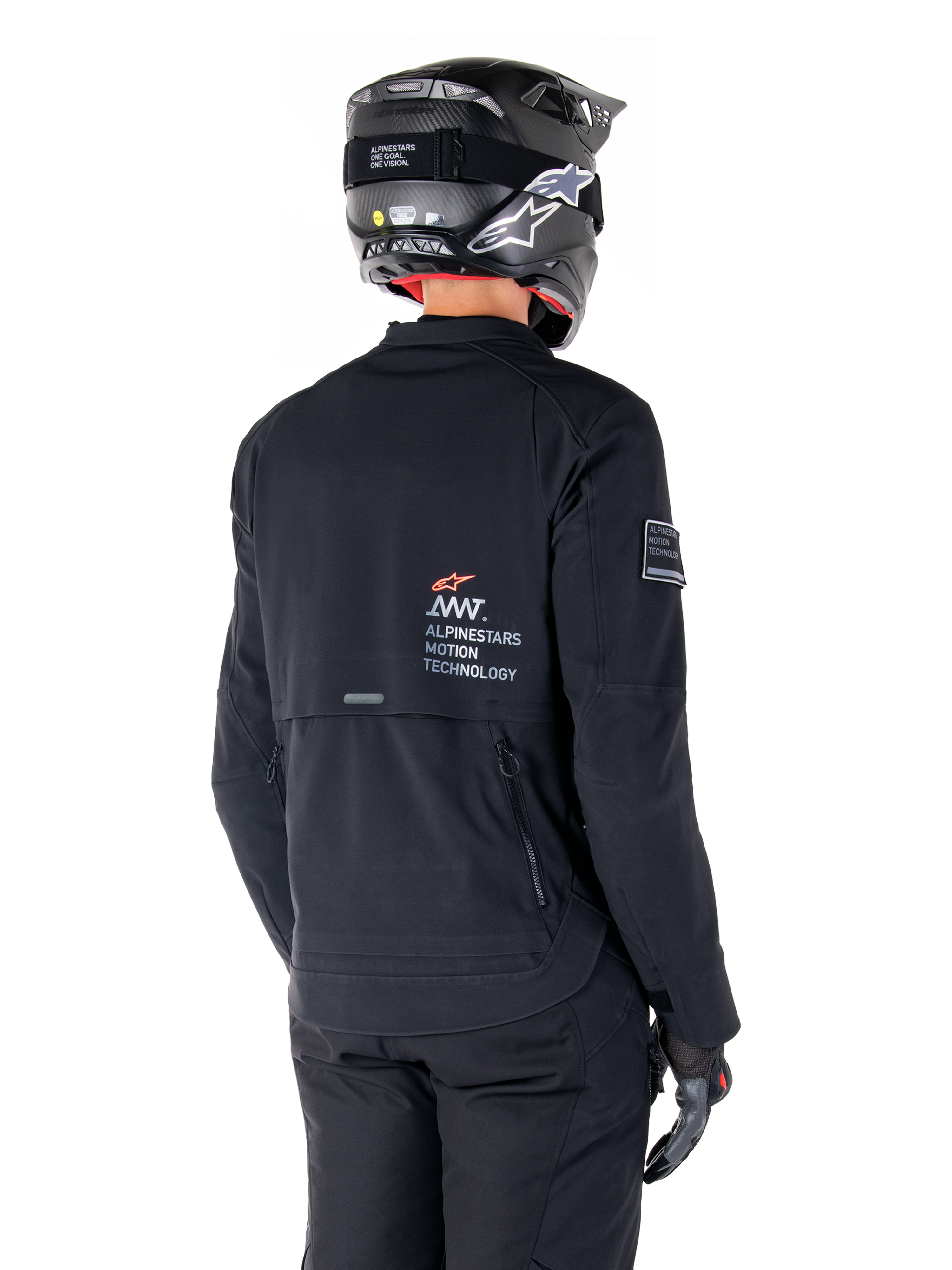 Vista trasera de un piloto con la chaqueta Alpinestars AMT-8 Stretch Drystar® XF en negro, con el logotipo 'AMT Alpinestars Motion Technology' en la espalda y ventilación técnica con cremallera, combinada con casco y guantes de moto negros