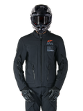 Chaqueta Alpinestars AMT-8 Stretch Drystar® XF, chaqueta de moto negra con logotipo naranja de Alpinestars y marca AMT en gris, cuello alto con cremallera frontal y ventilaciones, combinada con casco y guantes negros, equipamiento de protección para adventure touring