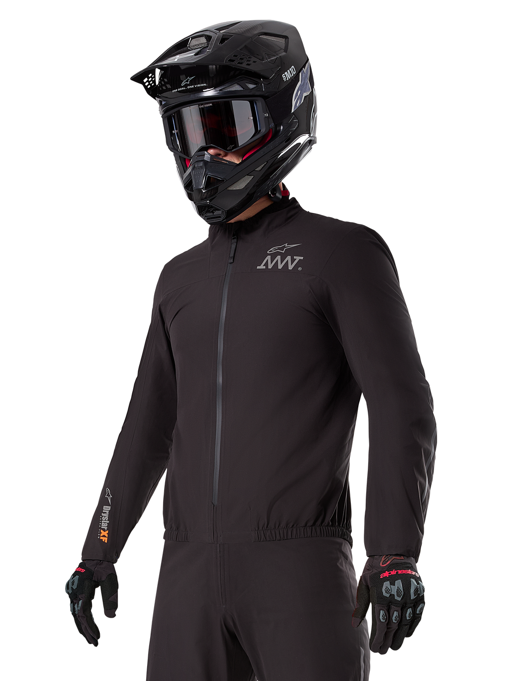 Piloto vistiendo el forro Alpinestars AMT-8 Stretch Drystar® XF, chaqueta elástica negra cortavientos e impermeable con logotipo AMT en el pecho y marca Drystar XF en la manga, combinada con casco de aventura negro y guantes protectores.