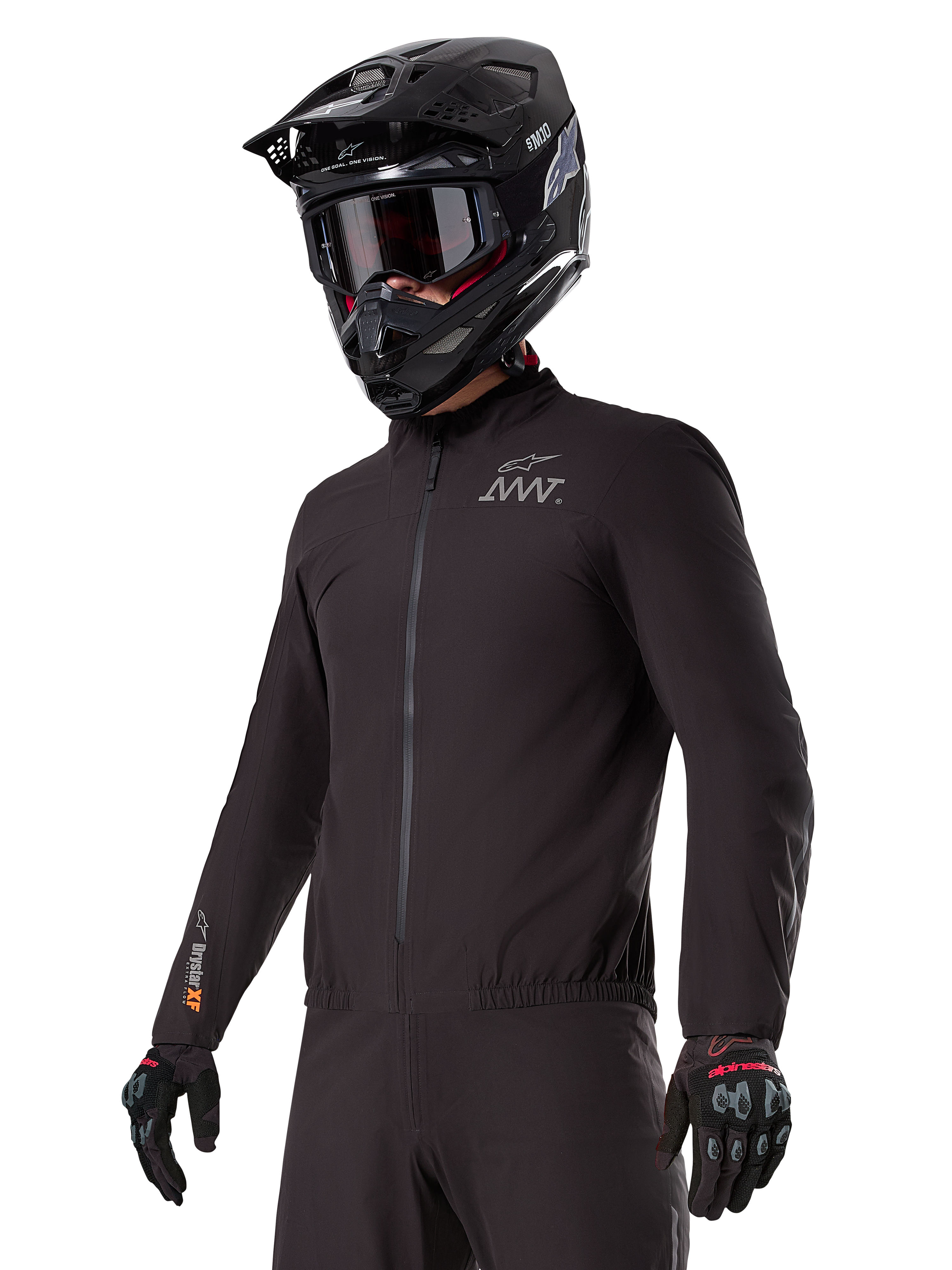 Piloto vistiendo el forro Alpinestars AMT-8 Stretch Drystar® XF, chaqueta elástica negra cortavientos e impermeable con logotipo AMT en el pecho y marca Drystar XF en la manga, combinada con casco de aventura negro y guantes protectores.