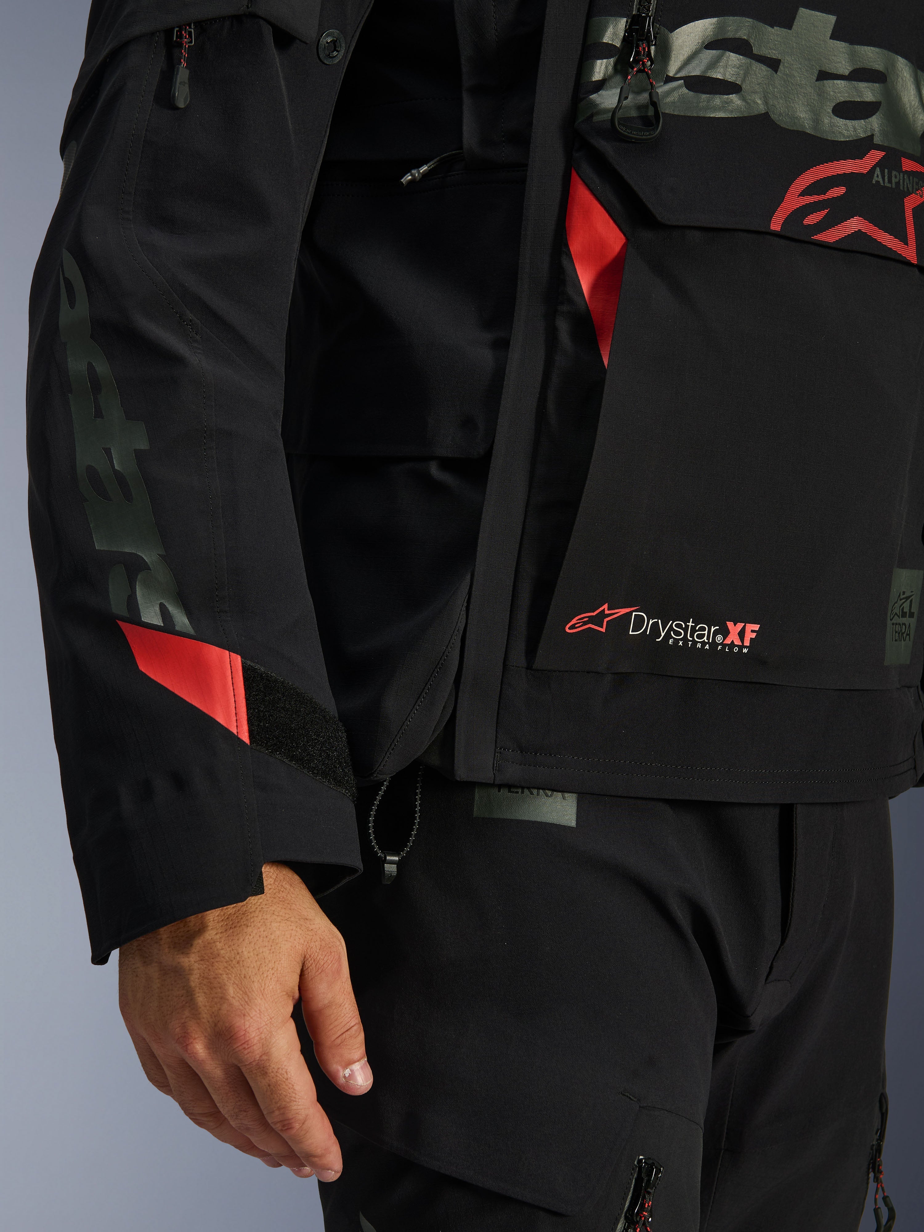 Chaqueta laminada Alpinestars Halo Pro Drystar® XF, chaqueta de moto, negra con detalles en rojo, primer plano con el logotipo Drystar® XF, textura técnica laminada y detalles ajustables en la manga para conducción de aventura