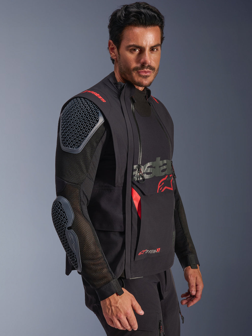 Chaqueta laminada Alpinestars Halo Pro Drystar® XF, negro y Dark Shadow, chaqueta de moto de aventura llevada por un modelo, configuración modular con mangas de malla y protecciones integradas en hombros y codos, acentos del logo en rojo y cremalleras impermeables técnicas.