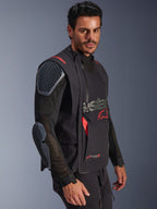 Chaqueta laminada Alpinestars Halo Pro Drystar® XF, negro y Dark Shadow, chaqueta de moto de aventura llevada por un modelo, configuración modular con mangas de malla y protecciones integradas en hombros y codos, acentos del logo en rojo y cremalleras impermeables técnicas.