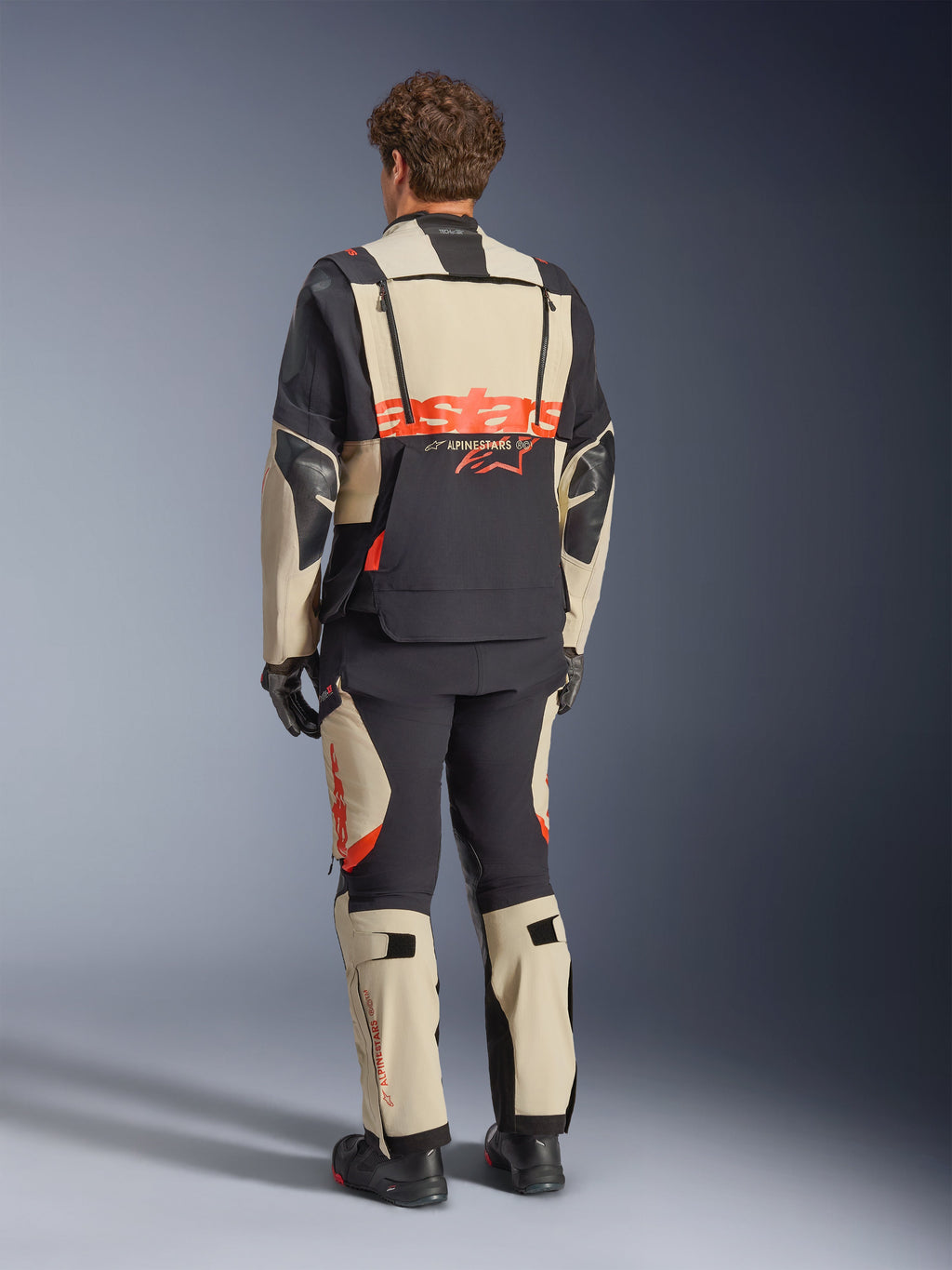 Chaqueta laminada Alpinestars Halo Pro Drystar® XF, Negro Mastic, vista posterior, chaqueta de moto de aventura con un gran logotipo 'astars' naranja en la parte trasera, usada con pantalones técnicos y botas a juego, diseño modular para terrenos versátiles