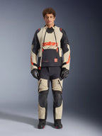 Chaqueta laminada Alpinestars Halo Pro Drystar® XF, Mastic Black, chaqueta de moto de aventura usada por un modelo con pantalones y guantes a juego, paneles textiles en color arena y negro con logotipos rojos llamativos, diseño modular para conducción todoterreno