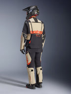 Chaqueta laminada Alpinestars Halo Pro Drystar® XF, Mastic Black, vista trasera de un piloto con el traje de aventura completo, pantalones a juego, casco de aventura negro y botas, con un llamativo logotipo rojo de Alpinestars en la espalda.