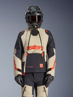Chaqueta laminada Alpinestars Halo Pro Drystar XF, chaqueta de moto de aventura en color Mastic Black y beige con detalles rojos, usada con equipo de protección completo incluyendo casco y guantes, con paneles de ventilación modulares y construcción laminada 3L.
