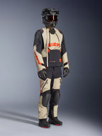 Chaqueta laminada Alpinestars Halo Pro Drystar® XF en color Mastic Black, chaqueta de moto adventure usada con pantalones a juego, casco integral, guantes y botas, con paneles en beige y negro con logotipos rojos y diseño técnico multiestación.