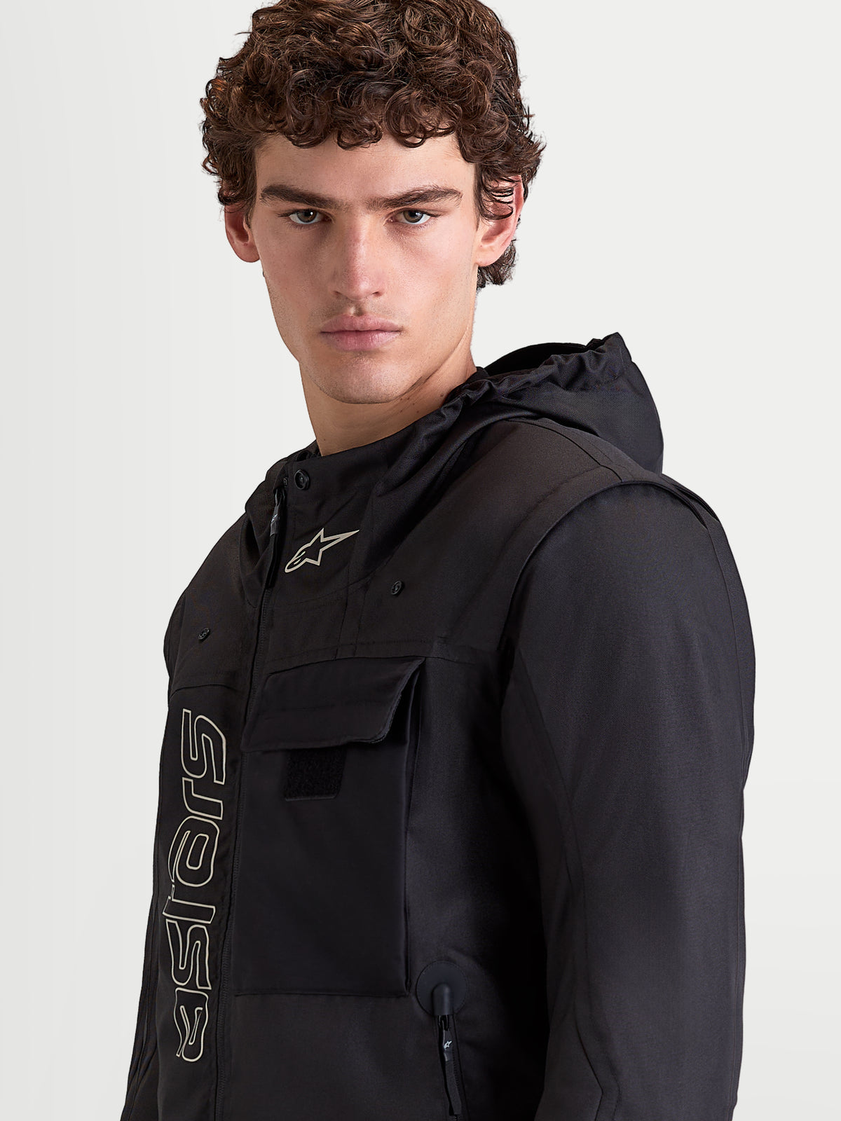 Alpinestars Morfex Parka Waterproof Jacket, chaqueta de moto urbana textil para hombre en color negro, retrato de cerca de un modelo vistiendo la chaqueta con capucha integrada y detalles de bolsillos en el pecho