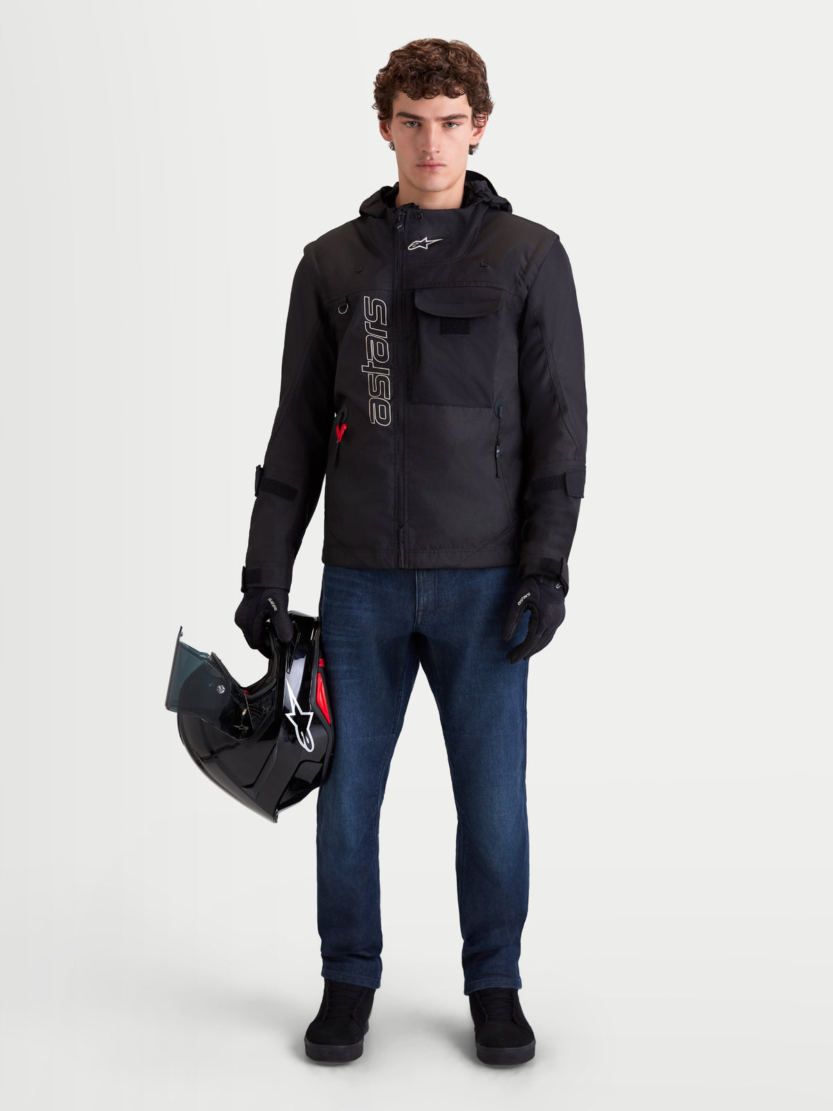 Alpinestars Morfex Parka Waterproof Jacket, men's urban motorcycle textile jacket in black, front view on a model wearing jeans and holding a helmet, showcasing modular design and integrated hood