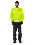 Chaqueta y pantalones Alpinestars Hurricane Rain V2, amarillo neón y negro, traje de lluvia impermeable para motocicleta usado con guantes y botas negras, con el logotipo de Alpinestars en el pecho y la pierna