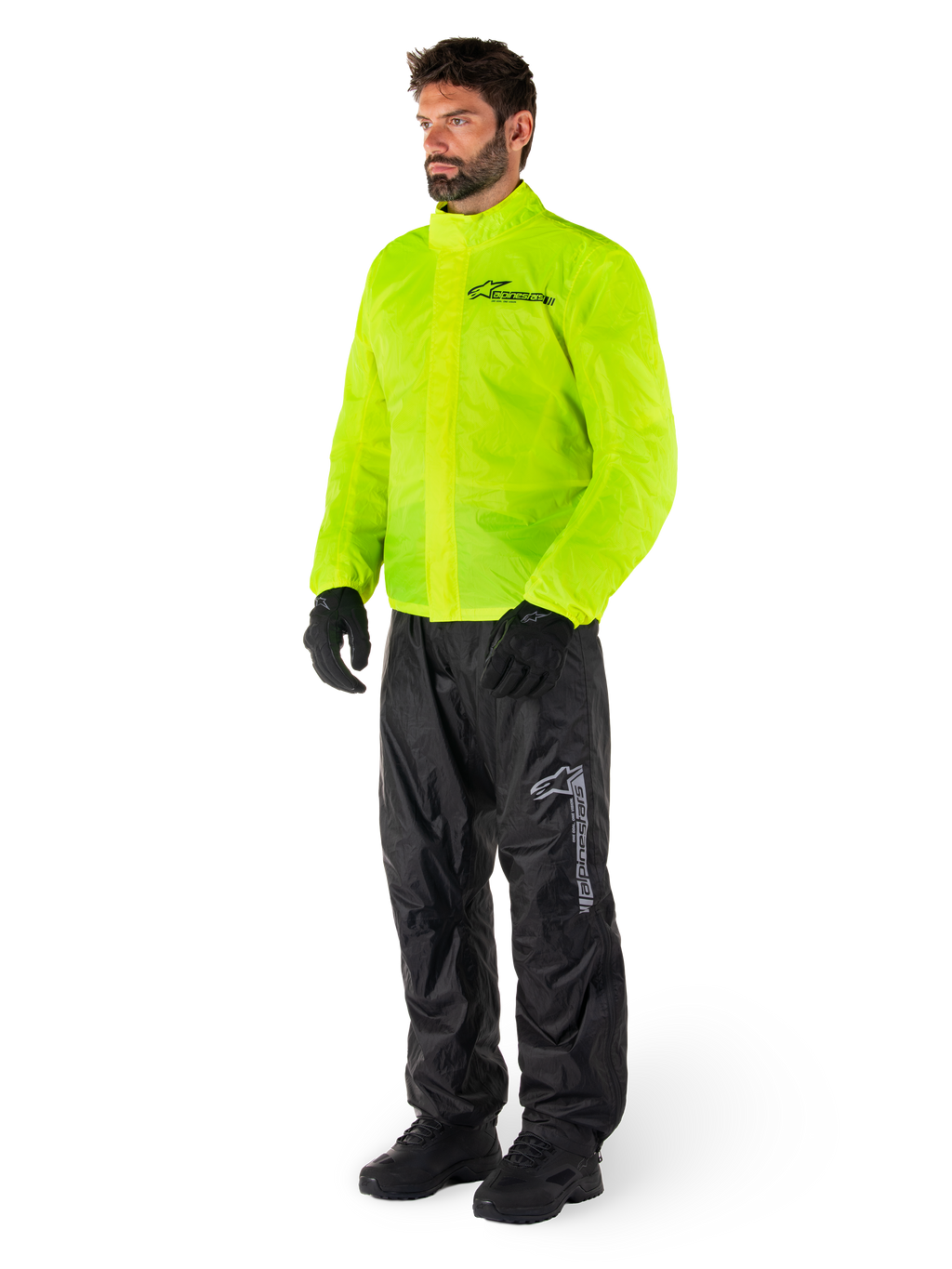 Hombre con chaqueta Alpinestars Hurricane Rain V2 en amarillo flúor y pantalones Hurricane Rain V2 en negro, equipo de lluvia impermeable y de alta visibilidad para motocicleta, con logotipos reflectantes en el pecho y el muslo, conjunto completo con guantes y botas negros