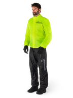 Hombre con chaqueta Alpinestars Hurricane Rain V2 en amarillo flúor y pantalones Hurricane Rain V2 en negro, equipo de lluvia impermeable y de alta visibilidad para motocicleta, con logotipos reflectantes en el pecho y el muslo, conjunto completo con guantes y botas negros