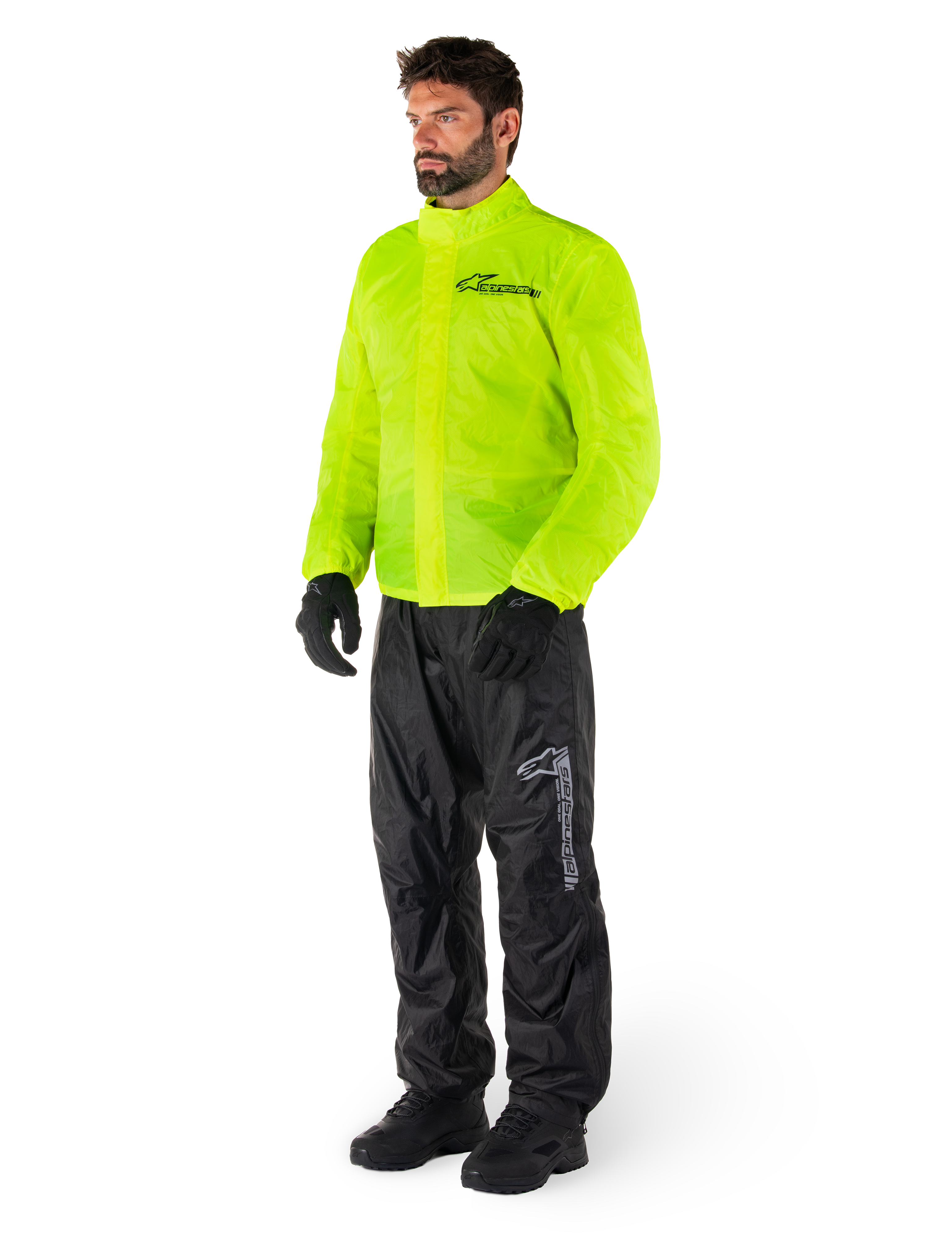 Hombre con chaqueta Alpinestars Hurricane Rain V2 en amarillo flúor y pantalones Hurricane Rain V2 en negro, equipo de lluvia impermeable y de alta visibilidad para motocicleta, con logotipos reflectantes en el pecho y el muslo, conjunto completo con guantes y botas negros