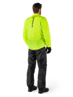 Persona desde atrás con la chaqueta Alpinestars Hurricane Rain V2 en amarillo flúor y el pantalón Hurricane Rain V2 en negro, logotipo vertical en la espalda de la chaqueta, equipo de lluvia impermeable para motocicleta con guantes y botas negros