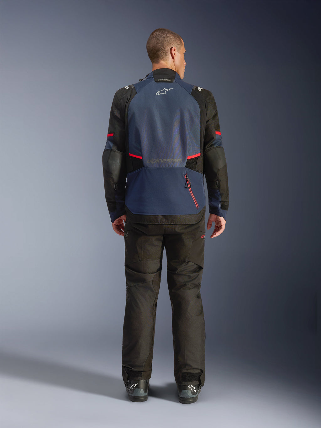 Chaqueta Alpinestars Andes V4 Drystar®, vista trasera, Night Navy y Mood Indigo con paneles negros y detalles rojos, combinada con pantalones negros a juego, con el logotipo de Alpinestars en la parte superior de la espalda y un compartimento trasero con cremallera.