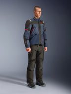 Modelo masculino luciendo la chaqueta Alpinestars Andes V4 Drystar® en Night Navy y Mood Indigo con paneles negros y detalles rojos, combinada con pantalones y botas de moto negros, equipamiento técnico de aventura y touring en un entorno de estudio.