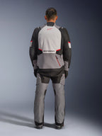 Chaqueta Alpinestars Andes V4 Drystar®, chaqueta de moto de aventura, gris oscuro, gris hielo, negro y rojo brillante, vista trasera de un motorista con pantalones a juego, con un gran panel posterior gris hielo con logotipo rojo, secciones de hombros reforzadas en negro y correas de cintura ajustables para turismo en cualquier clima.