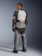 Chaqueta Alpinestars Andes V4 Drystar®, gris oscuro y gris hielo con detalles en negro y rojo brillante, vista trasera con panel gris claro y logo de estrella roja, combinada con pantalones de aventura a juego y guantes negros, equipamiento técnico de motociclismo para todo tipo de clima.
