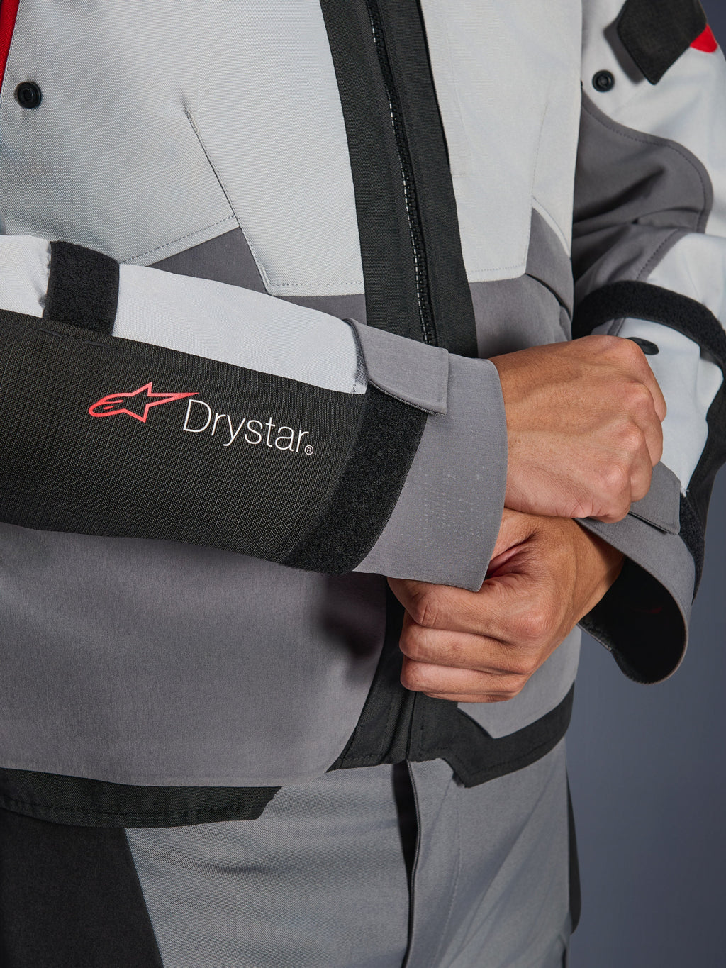 Detalle de primer plano de la manga de la chaqueta Alpinestars Andes V4 Drystar®, textil gris y negro, con el logotipo Drystar en rojo y blanco en el antebrazo, cierre de velcro ajustable en la muñeca, equipamiento impermeable de alto rendimiento para moto