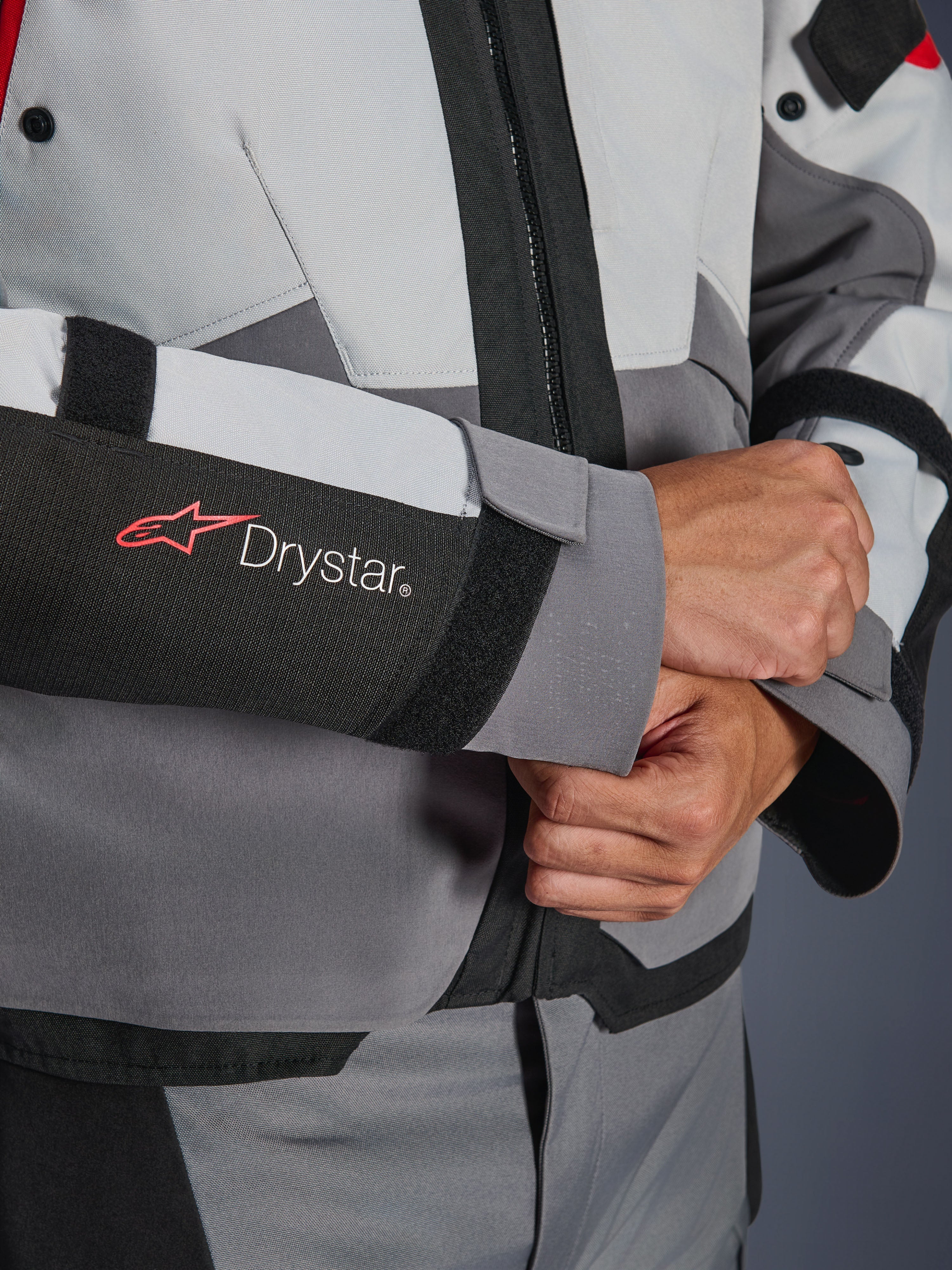 Detalle de primer plano de la manga de la chaqueta Alpinestars Andes V4 Drystar®, textil gris y negro, con el logotipo Drystar en rojo y blanco en el antebrazo, cierre de velcro ajustable en la muñeca, equipamiento impermeable de alto rendimiento para moto