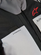 Chaqueta Alpinestars Andes V4 Drystar®, detalle en primer plano del pecho, paneles en gris oscuro y gris hielo con refuerzos textiles negros, con el logotipo de Alpinestars en rojo y un bucle para la manguera de hidratación con la etiqueta 'HYDRATION'