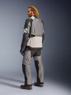Chaqueta Alpinestars Andes V4 Drystar®, gris oscuro, gris hielo, negro y amarillo flúor, vista trasera de piloto con pantalones y botas de adventure touring a juego, incluye paneles textiles reforzados, detalles en amarillo neón y marca Alpinestars, equipamiento de motociclismo para todo clima.
