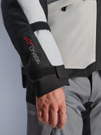 Chaqueta Alpinestars Andes V4 Drystar®, chaqueta de moto de aventura, paneles en color gris hielo y negro, primer plano de la manga con el logotipo Drystar® en rojo y correas ajustables, diseño textil funcional para conducir en cualquier clima