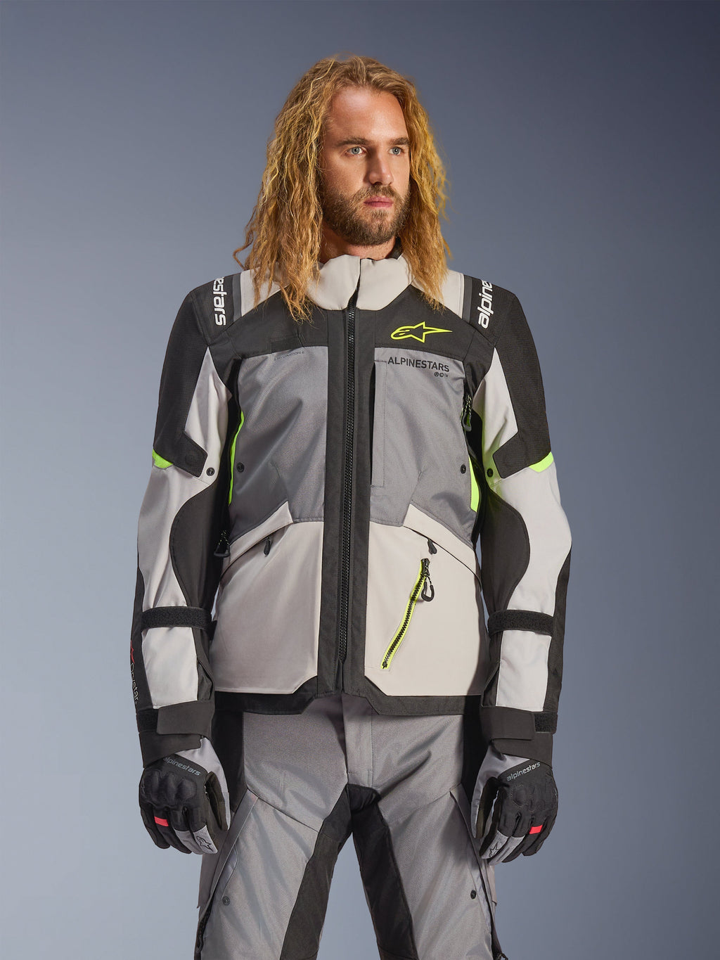 Chaqueta Alpinestars Andes V4 Drystar, chaqueta de moto para turismo de aventura, gris oscuro y gris hielo con detalles en amarillo neón, usada por un modelo con pantalones y guantes a juego, diseño textil multibolsillos para conducción en todo tipo de clima