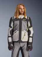 Chaqueta Alpinestars Andes V4 Drystar, chaqueta de moto para turismo de aventura, gris oscuro y gris hielo con detalles en amarillo neón, usada por un modelo con pantalones y guantes a juego, diseño textil multibolsillos para conducción en todo tipo de clima