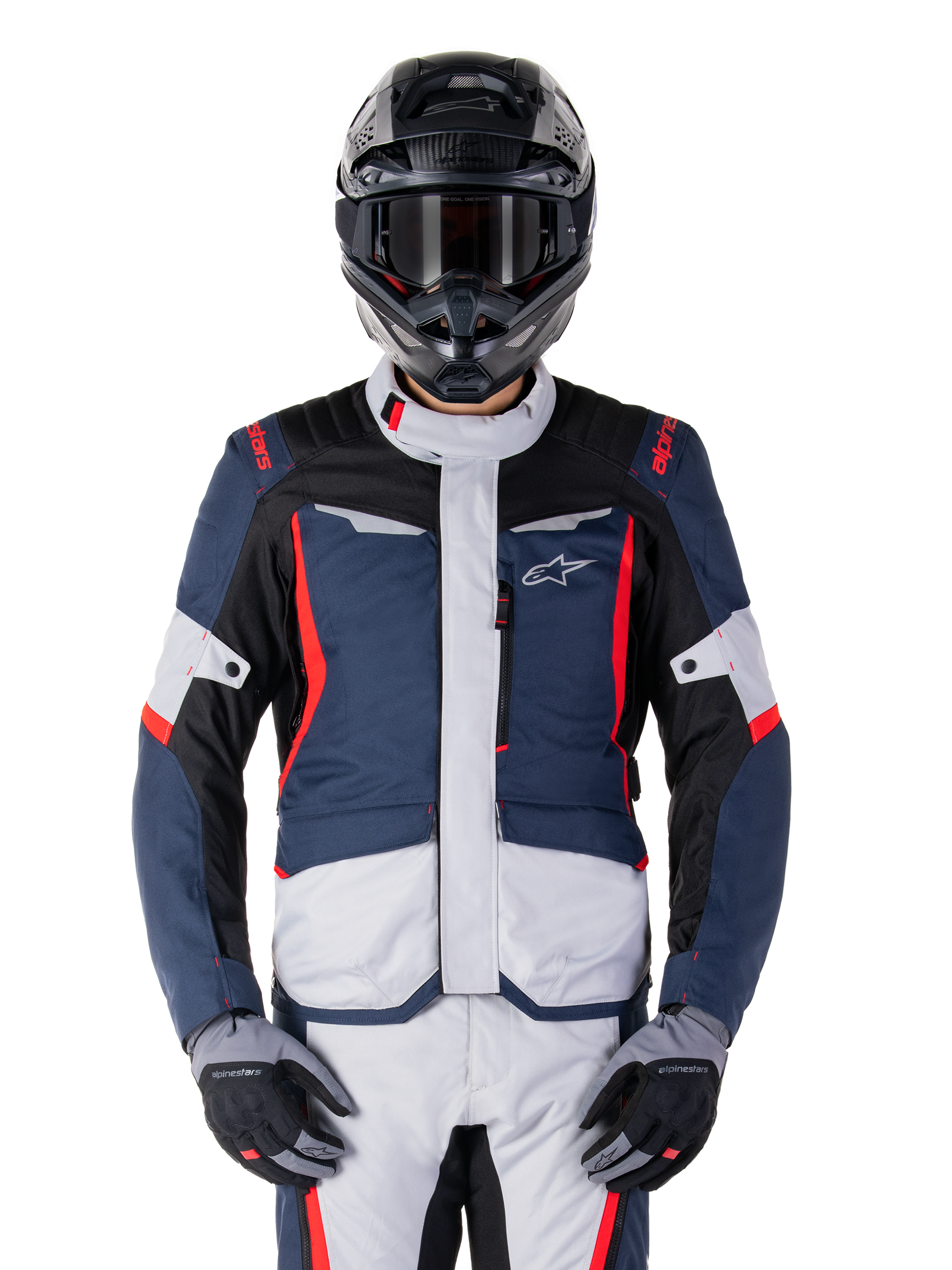 Chaqueta impermeable Alpinestars ST-1, chaqueta de moto para turismo de aventura, azul oscuro y negro con paneles gris claro y detalles en rojo brillante, usada con pantalones a juego y casco negro, con el logotipo de la estrella en el pecho y construcción textil duradera