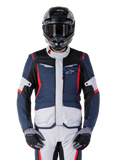 Chaqueta impermeable Alpinestars ST-1, chaqueta de turismo de aventura, azul oscuro, negro y rojo brillante, usada con casco de aventura negro y guantes grises, con paneles en gris claro y detalles rojos en hombros y cremalleras, diseño estilizado con la marca Alpinestars en el pecho, equipo impermeable duradero para motociclismo