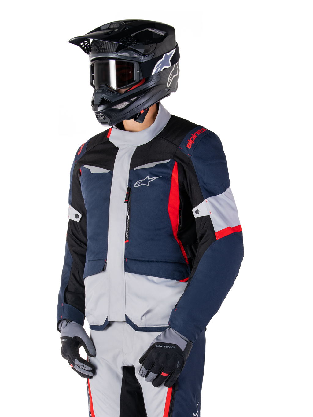 Chaqueta impermeable Alpinestars ST-1, chaqueta de moto adventure touring en azul oscuro, negro y rojo brillante, combinada con un casco negro y guantes grises, con un diseño moderno, bolsillos funcionales y el logotipo de Alpinestars.