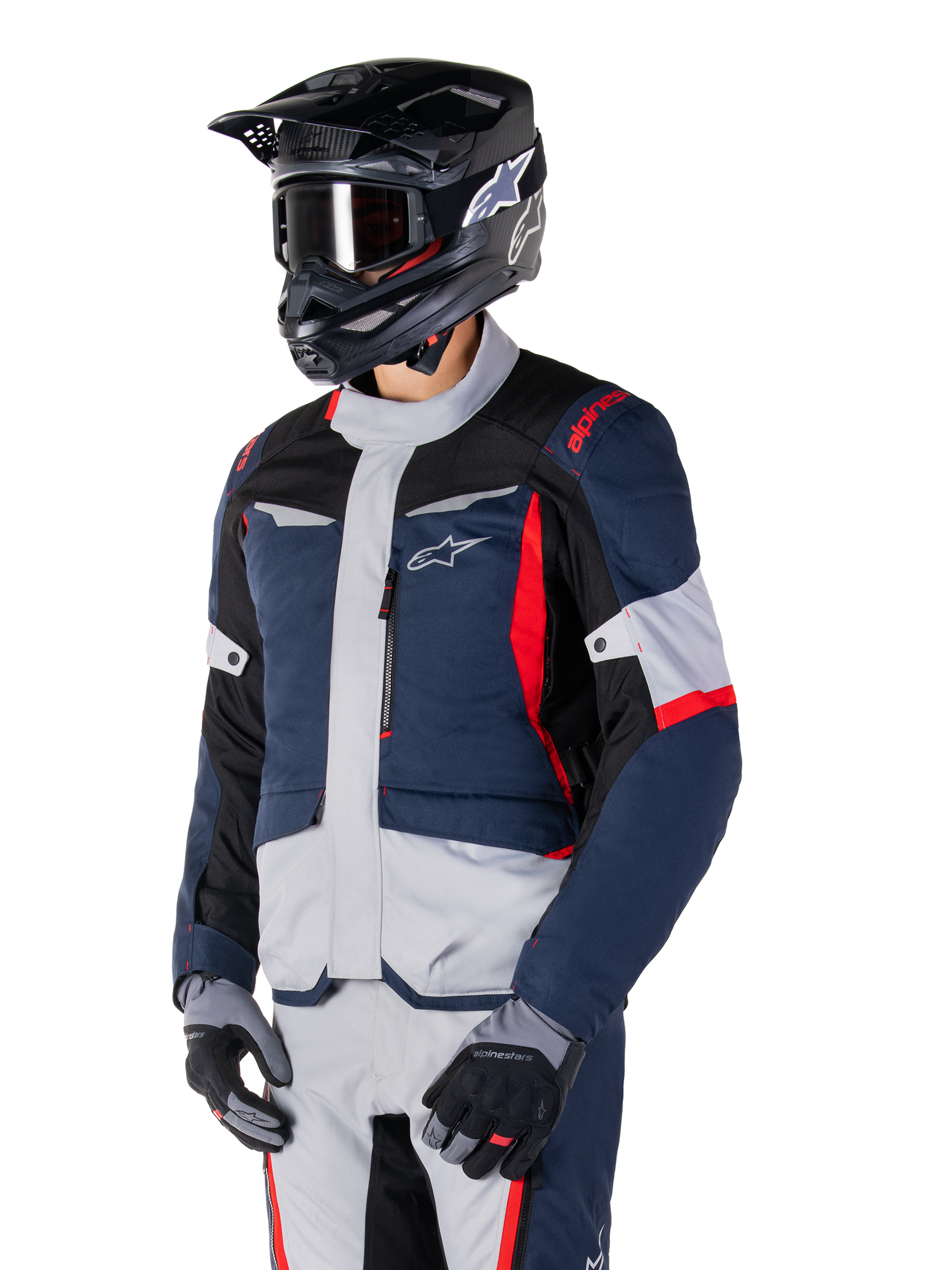 Chaqueta impermeable Alpinestars ST-1, chaqueta de moto adventure touring en azul oscuro, negro y rojo brillante, combinada con un casco negro y guantes grises, con un diseño moderno, bolsillos funcionales y el logotipo de Alpinestars.