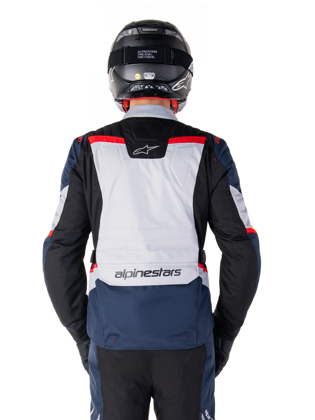 Chaqueta Alpinestars ST-1 Waterproof, azul oscuro, negro y rojo brillante, vista trasera que muestra el panel posterior en gris claro y la marca, chaqueta de moto adventure touring con casco y guantes negros, diseño aerodinámico para conducción en todo tipo de clima
