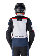 Chaqueta Alpinestars ST-1 Waterproof, azul oscuro, negro y rojo brillante, vista trasera que muestra el panel posterior en gris claro y la marca, chaqueta de moto adventure touring con casco y guantes negros, diseño aerodinámico para conducción en todo tipo de clima