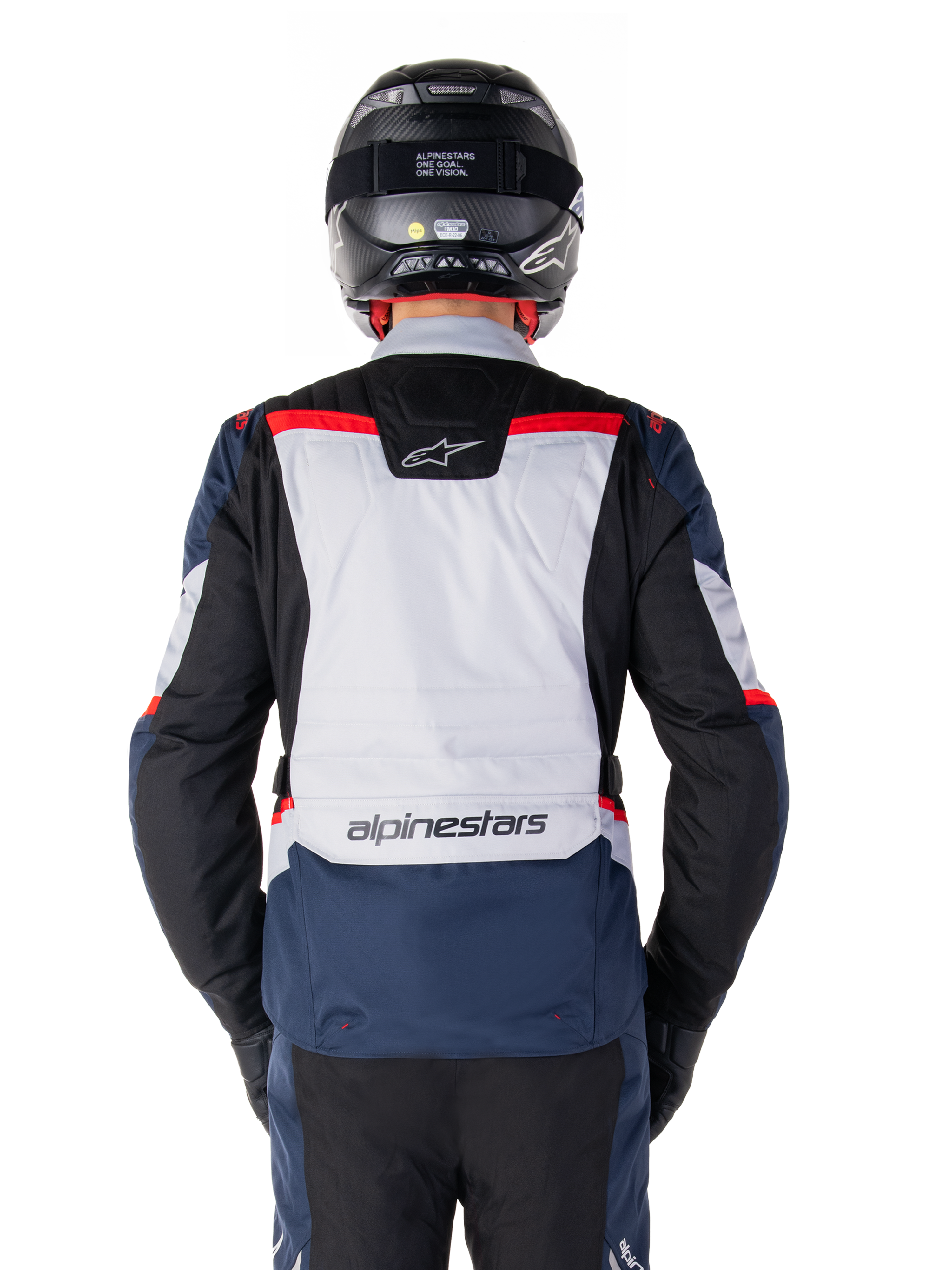 Chaqueta Alpinestars ST-1 Waterproof, azul oscuro, negro y rojo brillante, vista trasera que muestra el panel posterior en gris claro y la marca, chaqueta de moto adventure touring con casco y guantes negros, diseño aerodinámico para conducción en todo tipo de clima