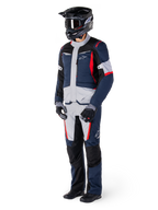 Chaqueta Alpinestars ST-1 Waterproof, chaqueta de turismo de aventura, azul oscuro, negro y rojo brillante, vestida por un piloto con pantalones a juego, casco adventure negro, guantes y botas, con paneles grises y detalles en rojo, diseño aerodinámico inspirado en el adventure con logotipos de Alpinestars