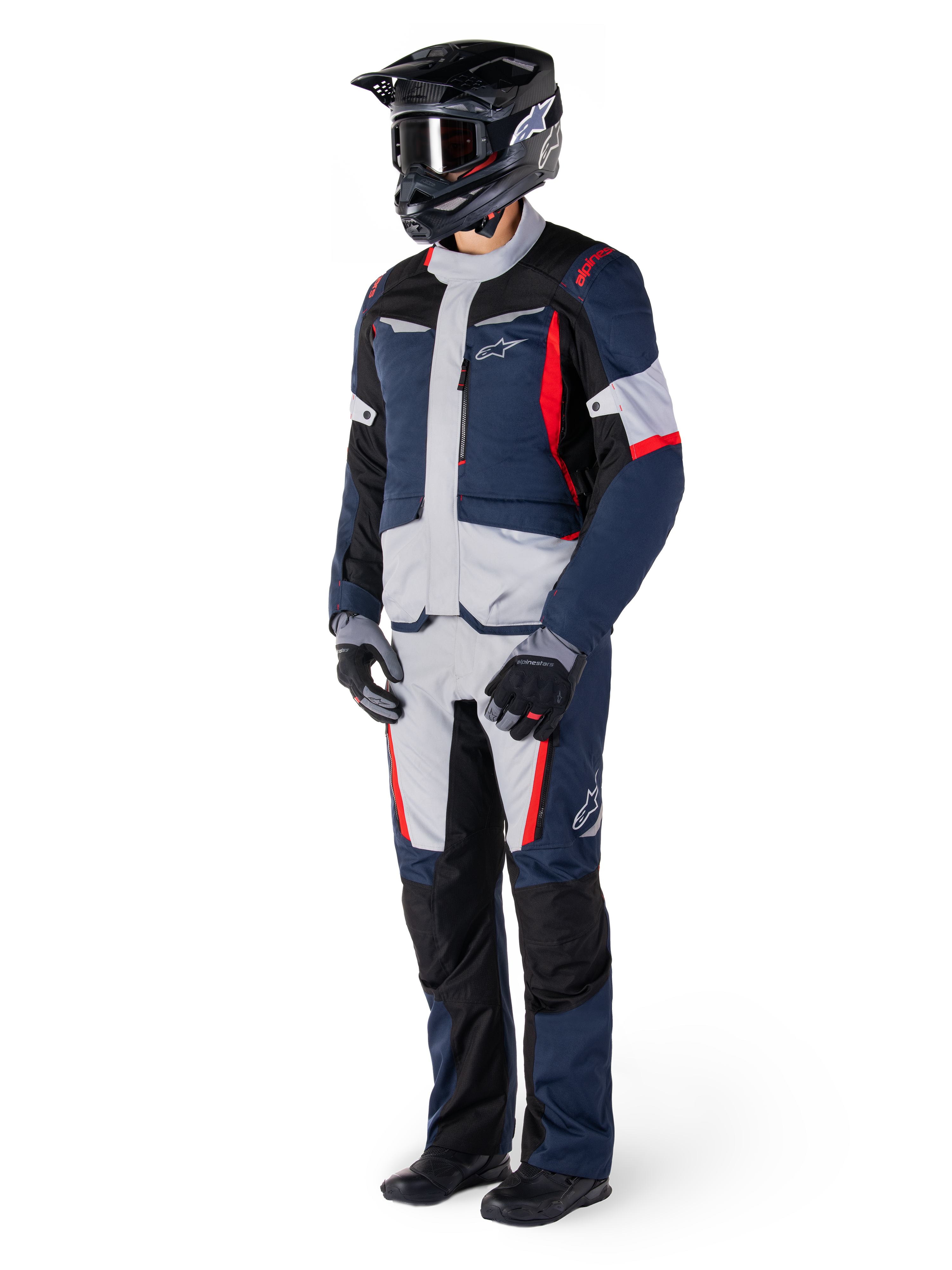 Chaqueta Alpinestars ST-1 Waterproof, chaqueta de turismo de aventura, azul oscuro, negro y rojo brillante, vestida por un piloto con pantalones a juego, casco adventure negro, guantes y botas, con paneles grises y detalles en rojo, diseño aerodinámico inspirado en el adventure con logotipos de Alpinestars