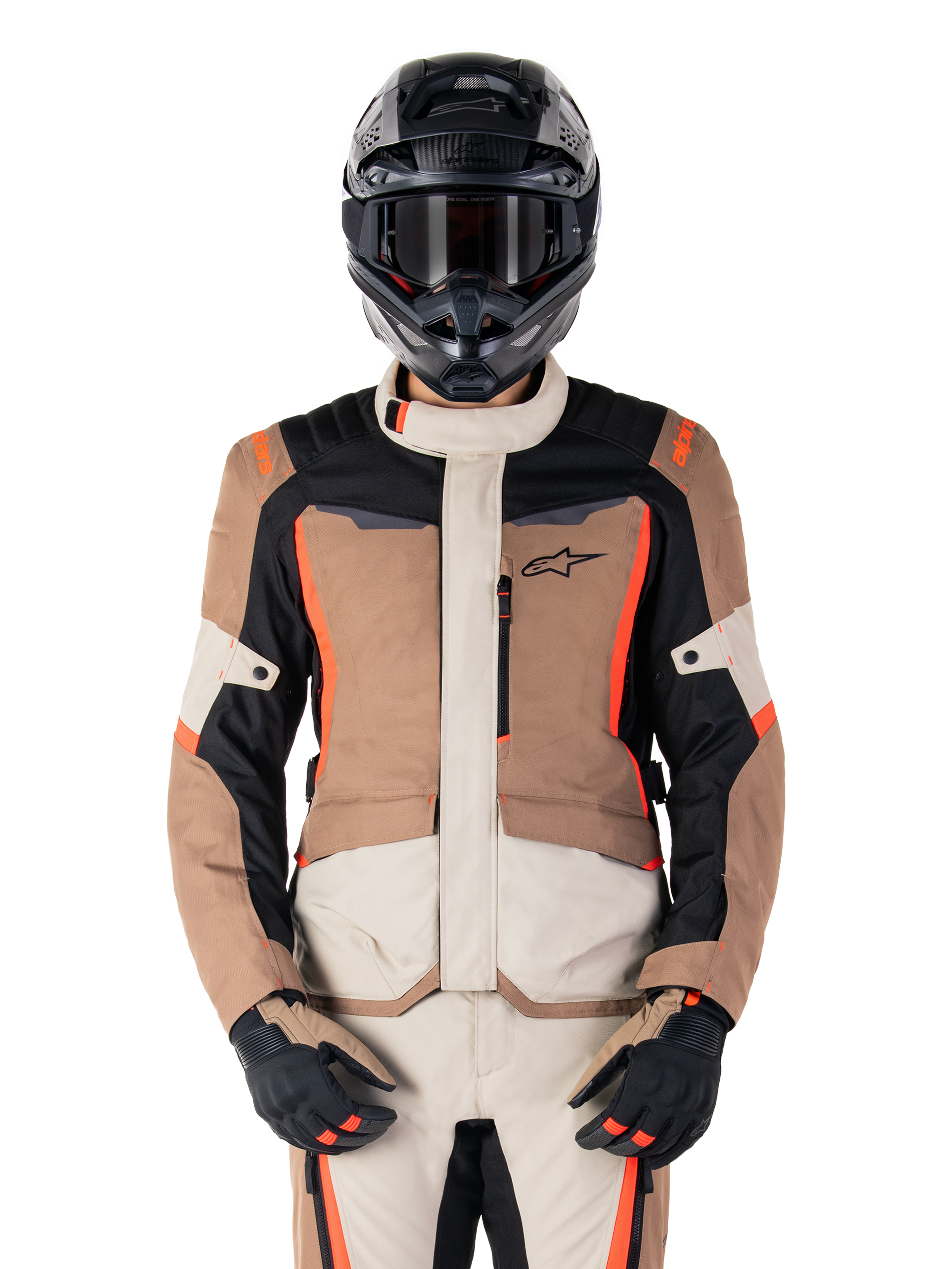 Chaqueta impermeable Alpinestars ST-1, Dark Khaki Sand Black Red Fluo, usada por un piloto con casco y guantes negros, equipamiento de touring de aventura con paneles beige y marrones y detalles en rojo flúor brillante, vista frontal sobre fondo blanco.