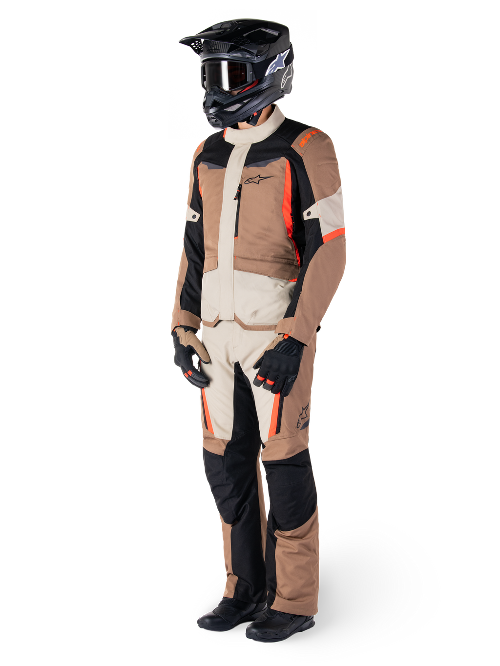 Chaqueta Alpinestars ST-1 Waterproof, Dark Khaki Sand Black Red Fluo, usada por un piloto con equipamiento completo de touring de aventura con pantalones a juego, casco negro, gafas, guantes y botas, conjunto técnico de moto para todo clima
