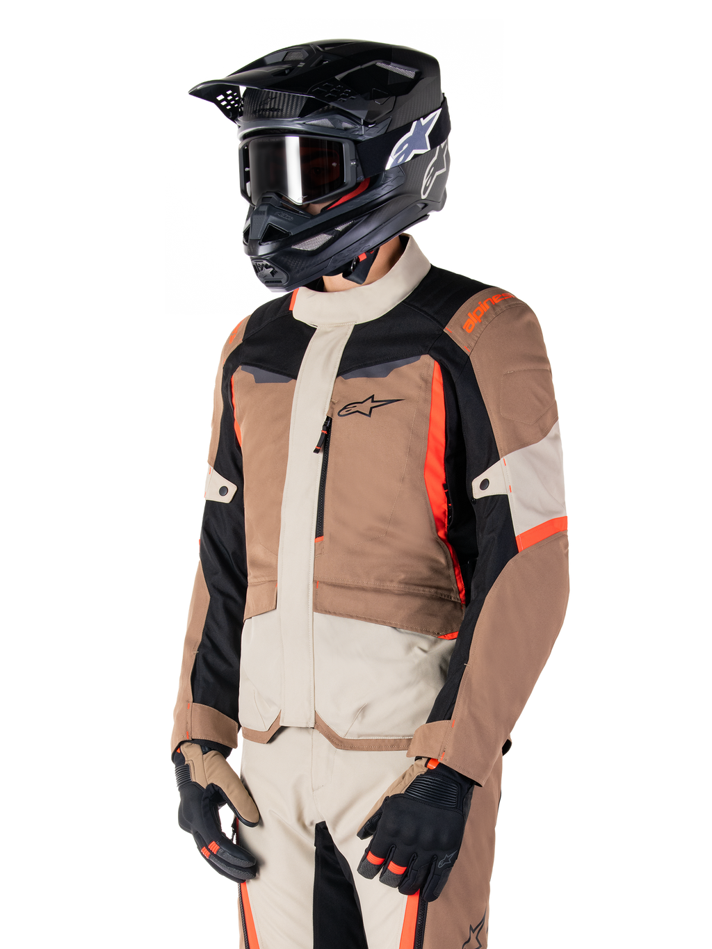 Chaqueta Alpinestars ST-1 Waterproof, chaqueta de touring de aventura, caqui oscuro, arena, negro y rojo flúor, usada por un piloto con casco de motocross negro y gafas, con un diseño de paneles múltiples, bolsillos cargo y el logo de Alpinestars en el pecho