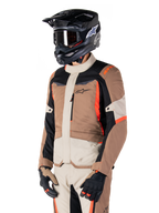 Chaqueta Alpinestars ST-1 Waterproof, chaqueta de touring de aventura, caqui oscuro, arena, negro y rojo flúor, usada por un piloto con casco de motocross negro y gafas, con un diseño de paneles múltiples, bolsillos cargo y el logo de Alpinestars en el pecho