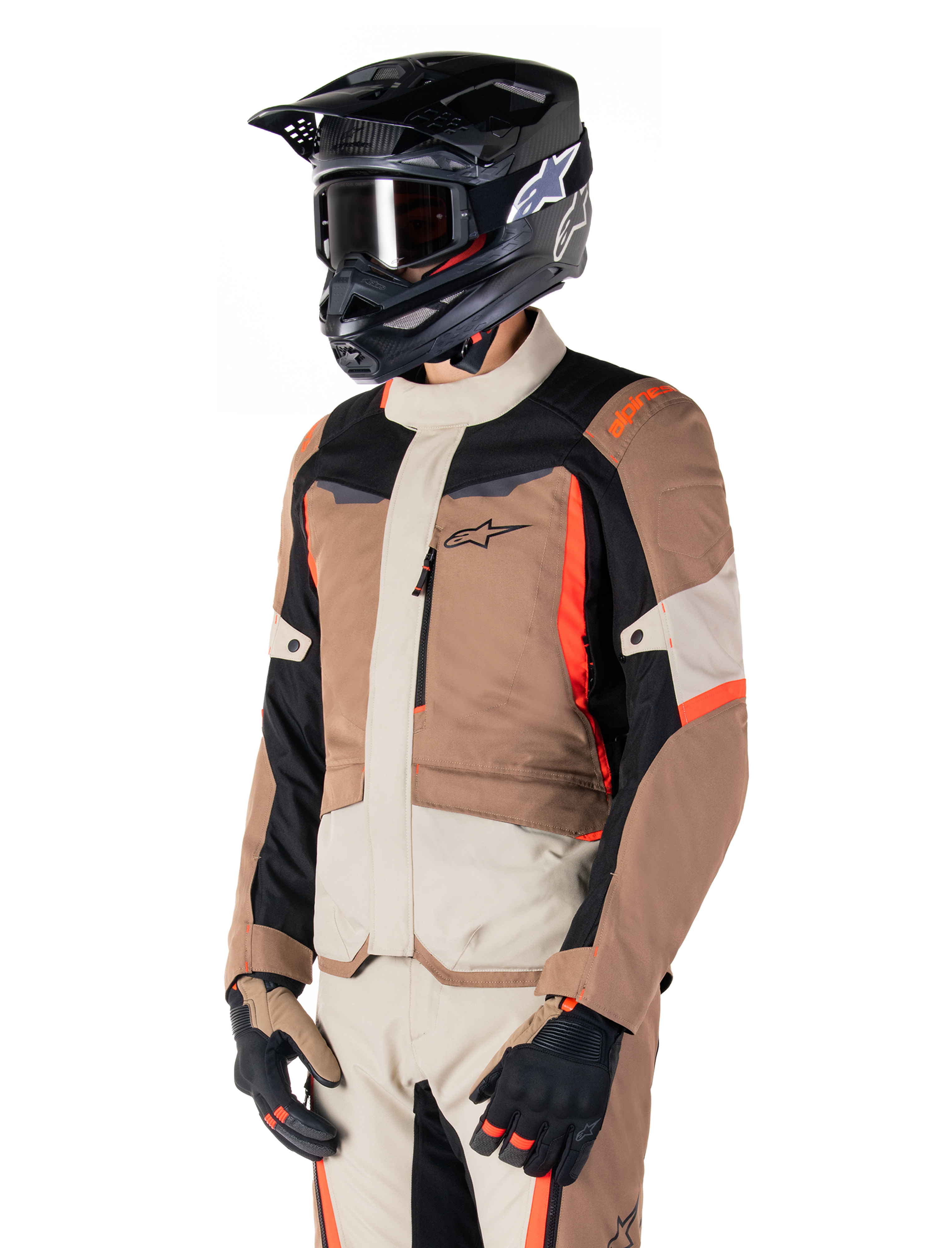 Chaqueta Alpinestars ST-1 Waterproof, chaqueta de touring de aventura, caqui oscuro, arena, negro y rojo flúor, usada por un piloto con casco de motocross negro y gafas, con un diseño de paneles múltiples, bolsillos cargo y el logo de Alpinestars en el pecho