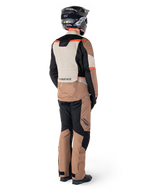 Chaqueta impermeable Alpinestars ST-1, chaqueta de touring de aventura, Dark Khaki Sand Black Red Fluo, vista trasera con pantalones a juego y casco negro, con paneles de bloques de color y detalles en rojo fluorescente.