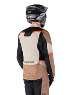 Chaqueta Alpinestars ST-1 Waterproof, chaqueta de touring de aventura, caqui oscuro, arena, negro y rojo flúor, vista trasera que muestra paneles textiles con bloques de color, detalles en rojo fluorescente y el logotipo de Alpinestars en la parte inferior de la espalda, usada por un piloto con un casco negro.