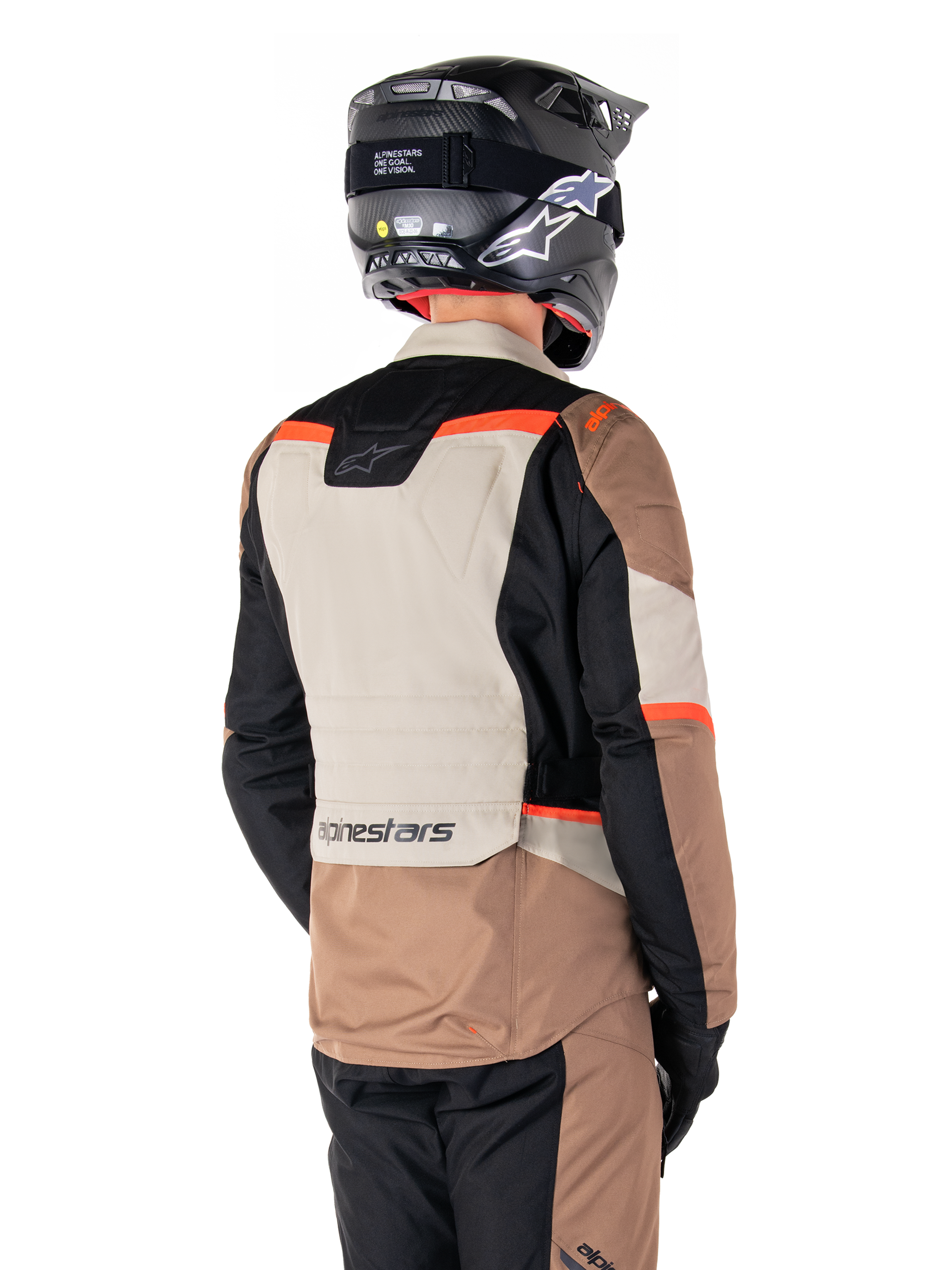 Chaqueta Alpinestars ST-1 Waterproof, chaqueta de touring de aventura, caqui oscuro, arena, negro y rojo flúor, vista trasera que muestra paneles textiles con bloques de color, detalles en rojo fluorescente y el logotipo de Alpinestars en la parte inferior de la espalda, usada por un piloto con un casco negro.