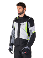 Alpinestars ST-1 Waterproof Jacket, Ice Gray Black Yellow Fluo, worn by a man with matching gloves and black pants, featuring gray torso panels with fluorescent yellow accents, black shoulders with white branding, adventure touring design for road riding