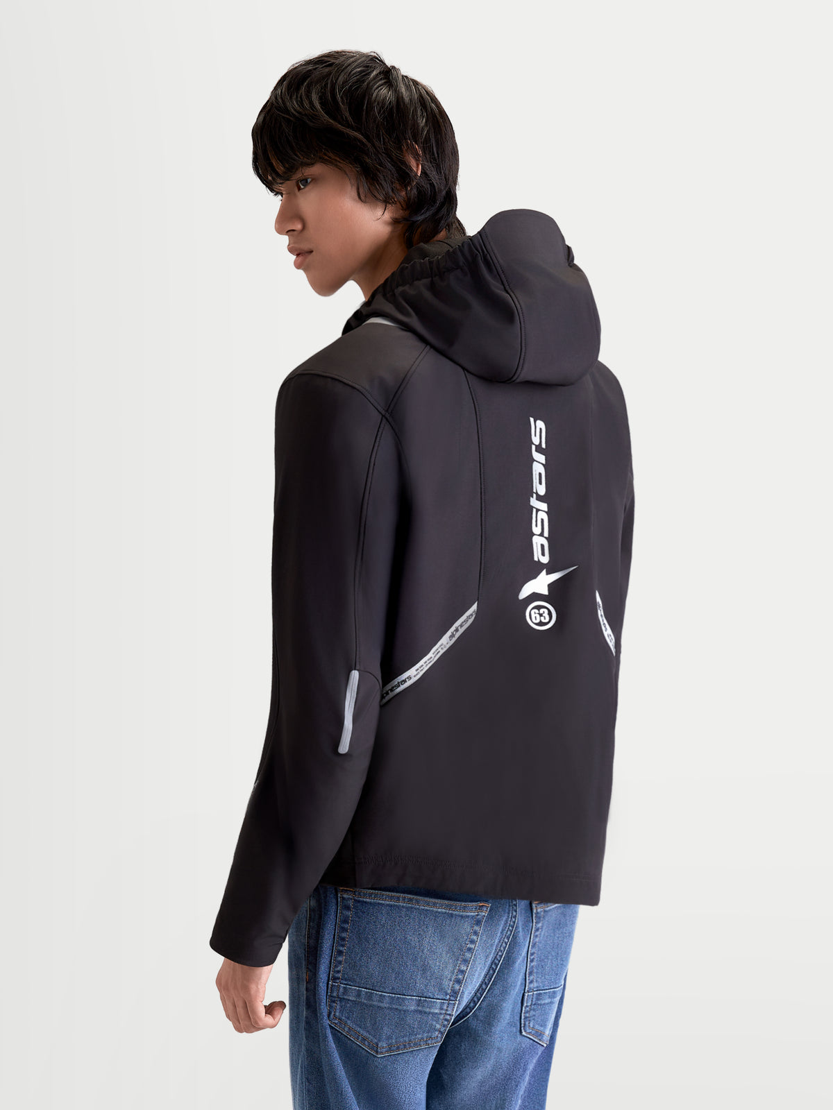 Alpinestars C 5 Drystar chaqueta de moto urbana contemporánea para hombre en negro, vista trasera de tres cuartos en un modelo que muestra capucha integrada, detalles reflectantes y logotipo vertical en la espalda